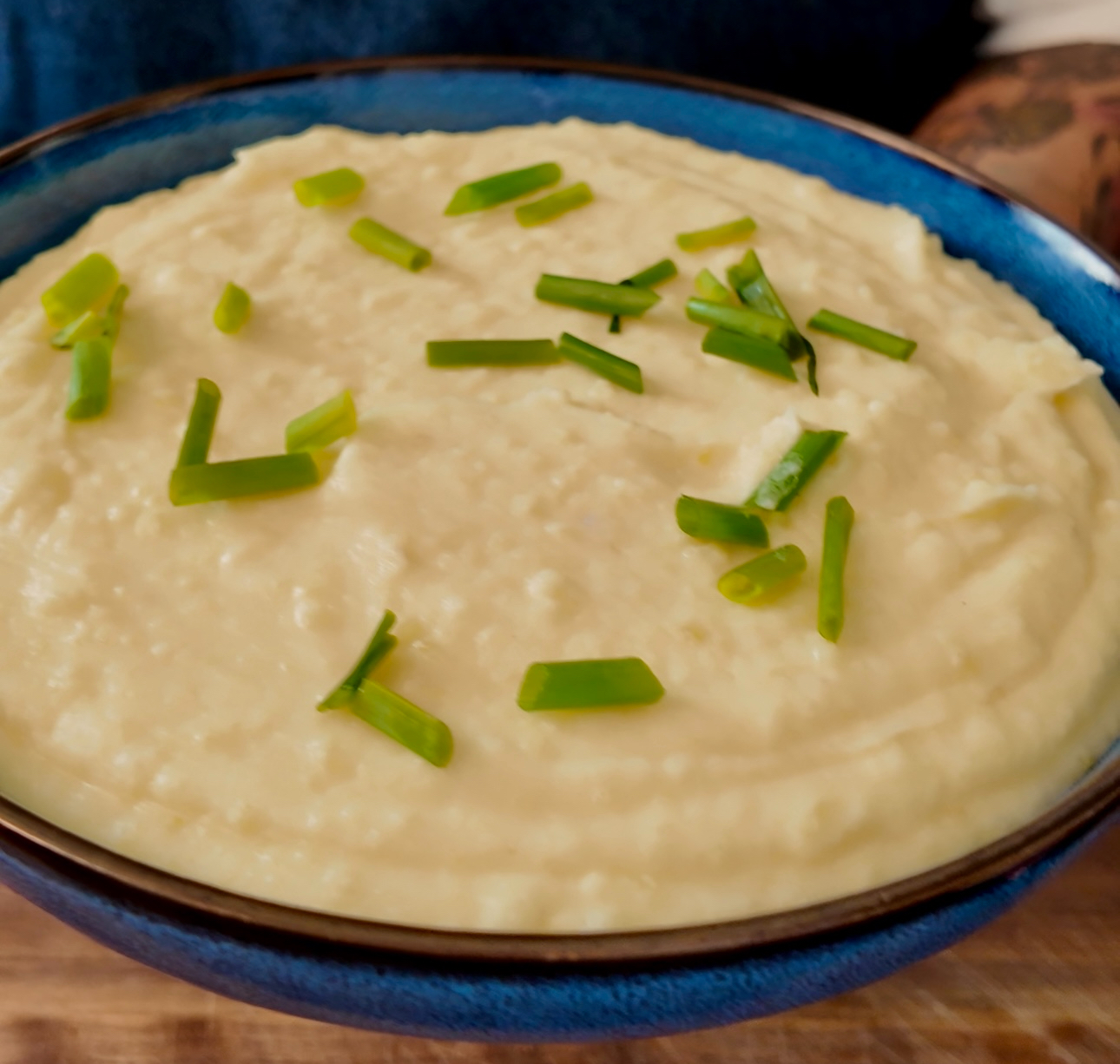 homemade mashed potatoes in a blue bowl garnished with fresh chives